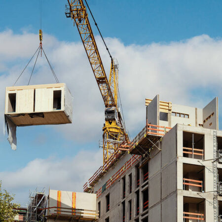 Crane lifting a wooden building module to its position in the structure.